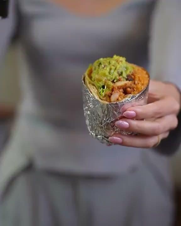 Warm white queso poured over a foil-wrapped Santa Fe burrito